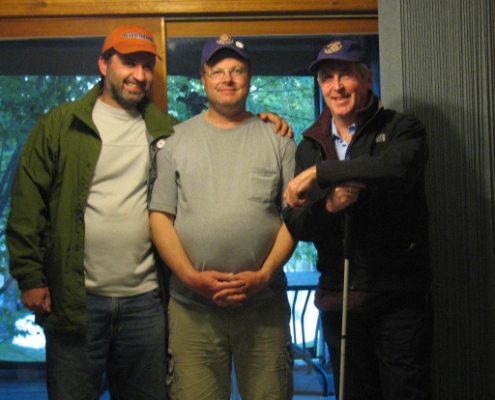 Three men standing indoors, wearing hats.