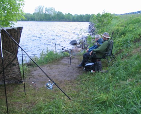 Two people fishing by a lakeside.
