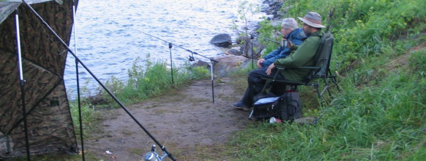 Two people fishing by a lakeside.