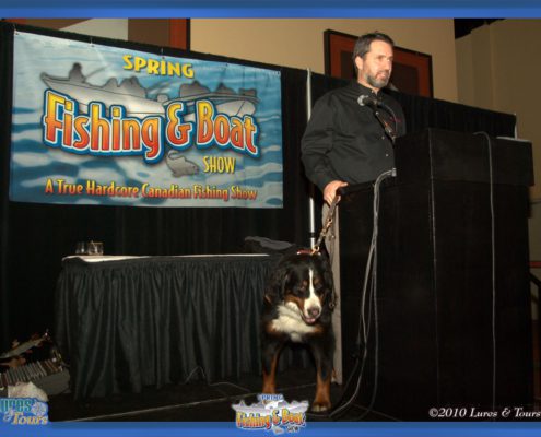 Man and dog at fishing show podium.