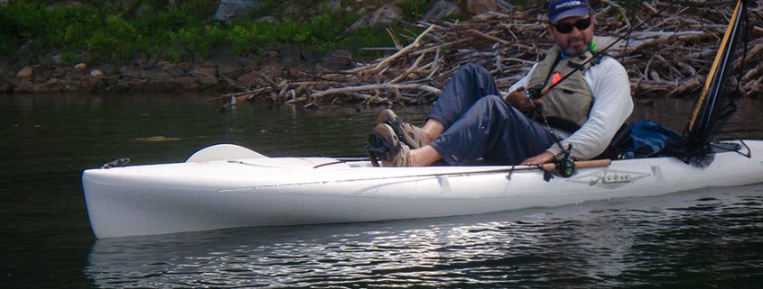 Man resting on a kayak in calm water surrounded by nature.
