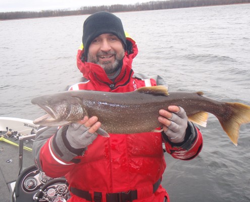 Person in red jacket holding a large fish by the water.