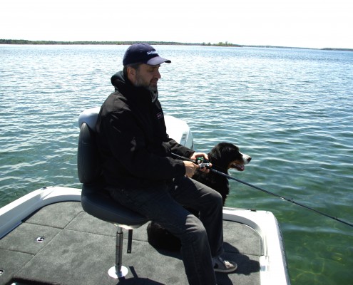 Man sitting on a dock by the water with a dog.