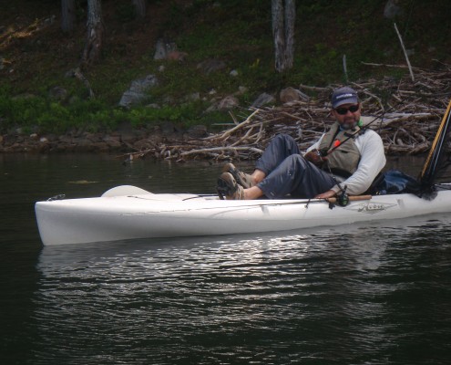Two people paddling a kayak on calm water near a forest.