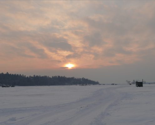 Snowy landscape with sunset and cloudy sky.