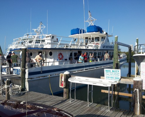A large yacht docked at a marina with people on board and walking nearby.