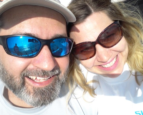 A happy couple wearing sunglasses and smiling in bright sunlight.