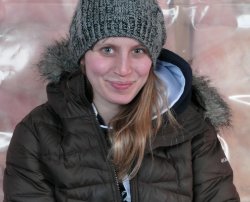 A young woman in winter clothing smiling outdoors in snowy weather.