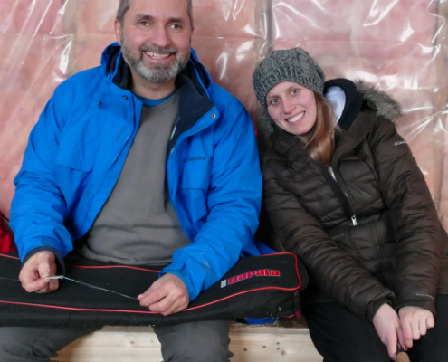 Two people sitting together on a bench, smiling at the camera.