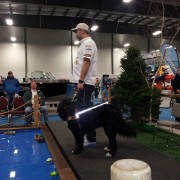 A man balances on a slackline indoors while another watches.