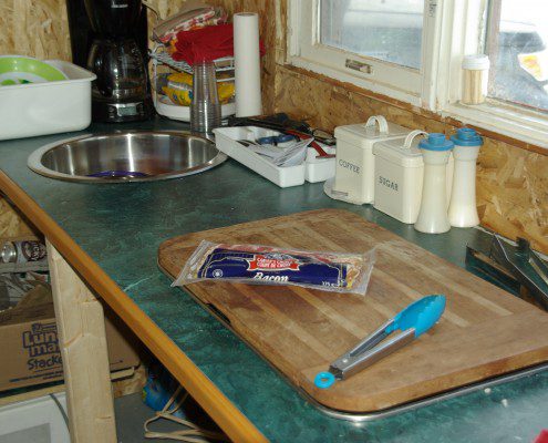 A cluttered kitchen countertop with utensils and food items.