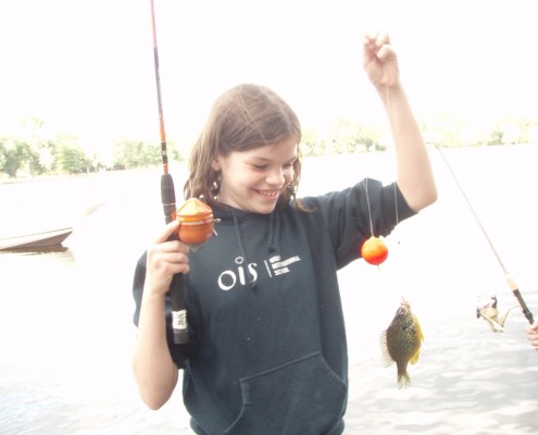 A child joyfully holding a fishing line with a small fish.