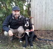 Man crouching beside a black and white dog outdoors.