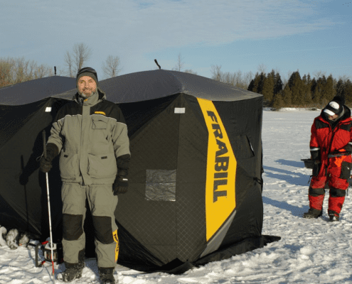 Two people standing beside a portable ice fishing shelter on snow.