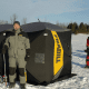 Two people standing beside a portable ice fishing shelter on snow.