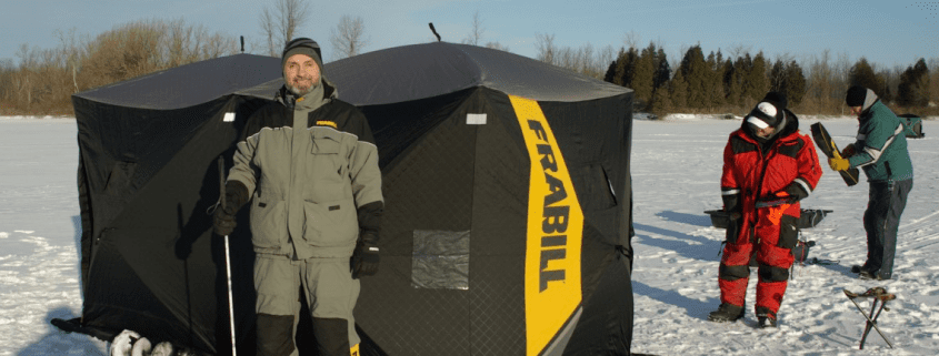 Two people standing beside a portable ice fishing shelter on snow.
