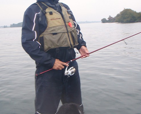 Person fishing on a calm lake with scenic background.