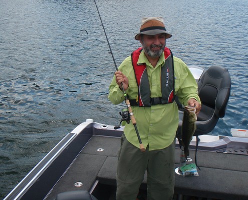 Man in fishing gear holding a caught fish on a boat.