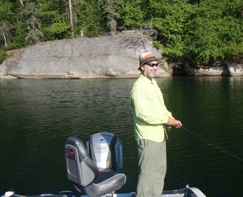 Person fishing by a rocky lakeshore on a sunny day.