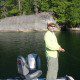 Person fishing by a rocky lakeshore on a sunny day.