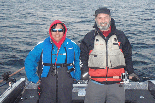 Two smiling men in fishing gear posing together outdoors.