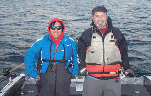 Two smiling men in fishing gear posing together outdoors.