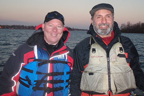 Two men smiling outdoors in fishing gear.