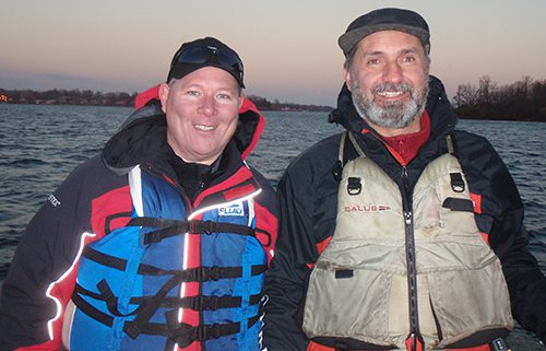 Two men smiling outdoors in fishing gear.