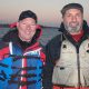 Two men smiling outdoors in fishing gear.