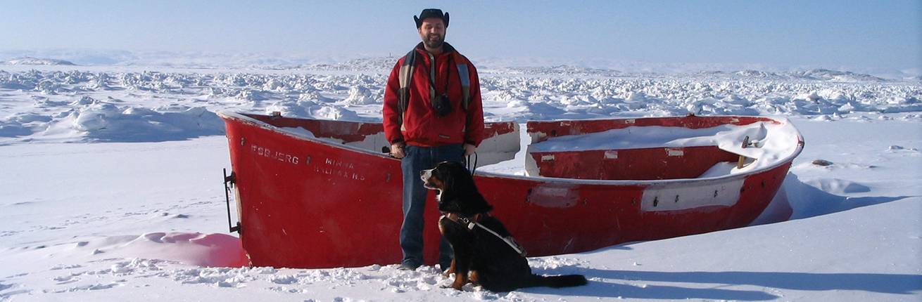 Lawrence with his Guide dog standing next to a traditional boat used by Inuit hunters