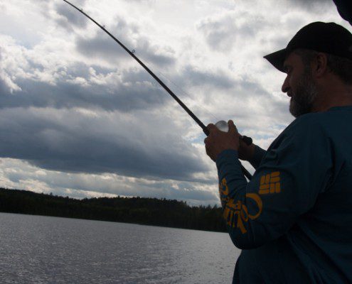 Person fishing on a lake during cloudy weather.