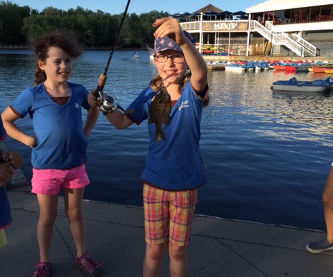 Two children holding up caught fish by a dock in the evening.