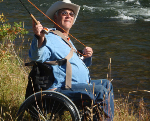 Man in a wheelchair holding a fish by a river.
