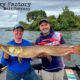 Two men proudly holding a large fish on a boat.