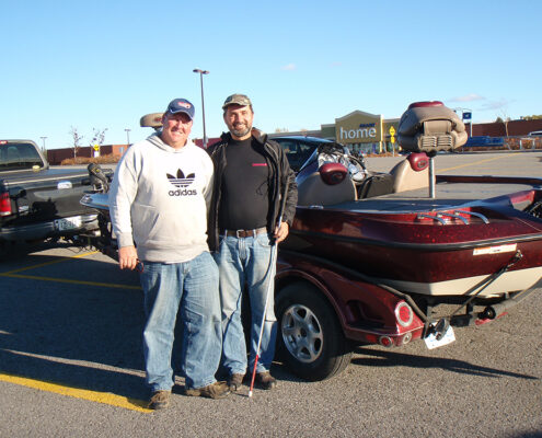 Two men posing next to a classic red convertible car in a parking lot.