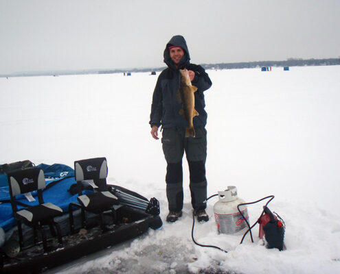 Person dressed for cold weather stands on snowy terrain with equipment nearby.