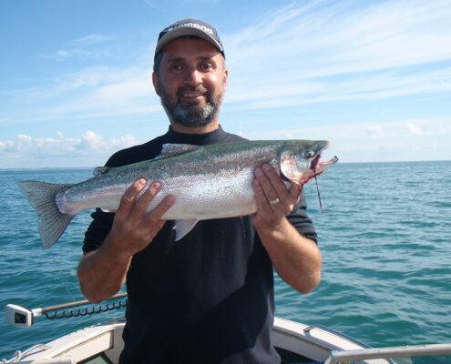 Man holding a large fish on a boat under a clear sky.