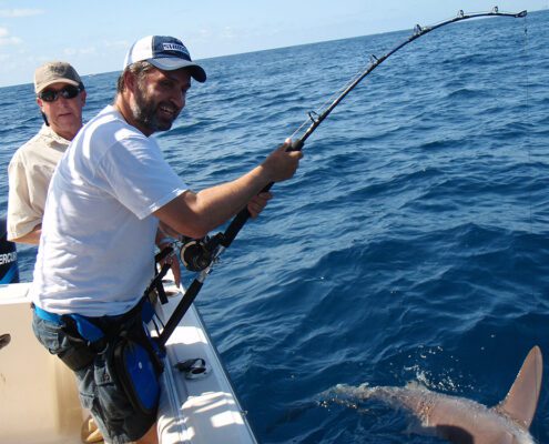 Man fishing on a boat in the open ocean under clear skies.