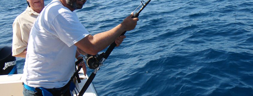 Man fishing on a boat in the open ocean under clear skies.