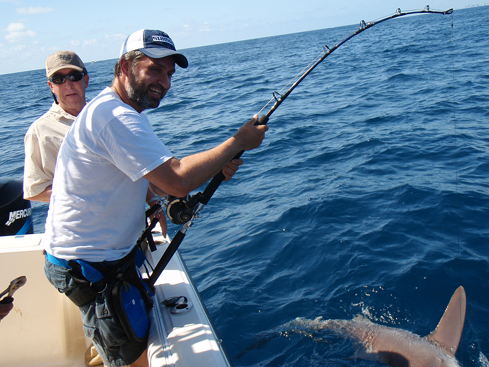 Man fishing on a boat in the open ocean under clear skies.