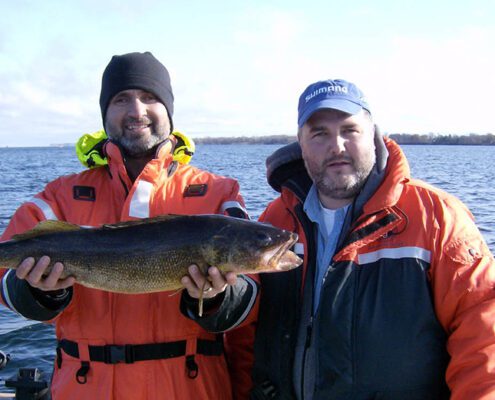 Two men in outdoor gear holding a large fish, smiling.