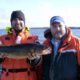 Two men in outdoor gear holding a large fish, smiling.
