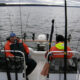 Two sailors on a small boat navigating calm waters.