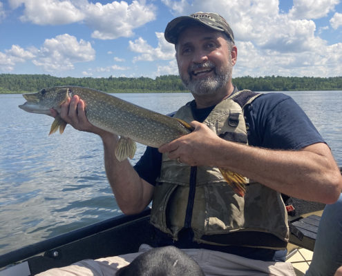 Man proudly holding a large fish on a boat under a blue sky.