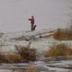 A person walking on a snow-covered landscape with patches of grass.
