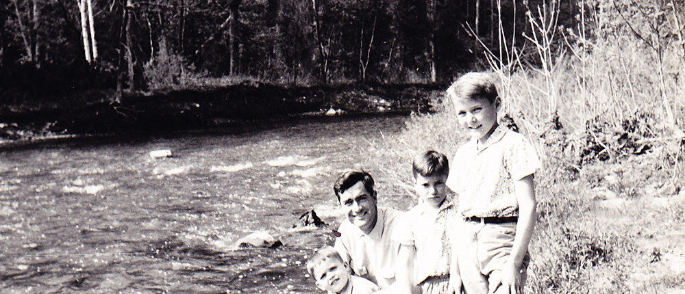 Photo of Dad holding Lawrence with Marc and Thomas standing on the shore