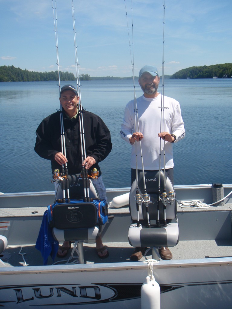 Two fishermen proudly display their catches on a boat in calm waters.