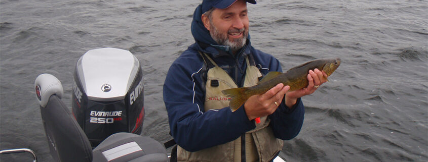 A man holding a fish on a boat near a body of water.