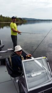 Two men fishing on a boat in calm waters.