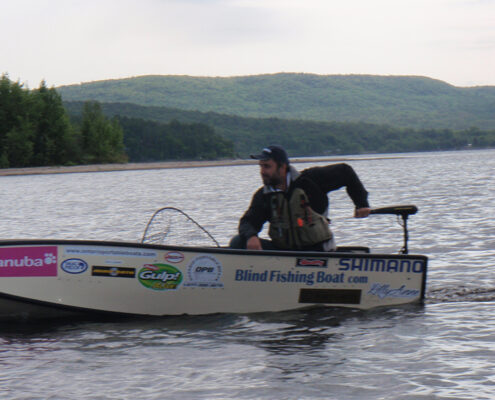 Person fishing on a small boat in a calm lake with hills in the background.